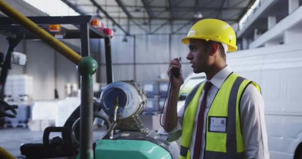 Vue latérale rapprochée d'un jeune ouvrier d'entrepôt asiatique debout dans une baie de chargement d'entrepôt parlant sur une radio bidirectionnelle. 4k 