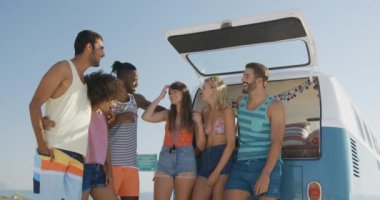 Genç yetişkin arkadaşlar bir plajda bir kamp minibüsü açık çizme tarafından duran bir çok ırklı grup ön görünümü konuşma ve gülüyor. Arkadaşlarla yaz eğlencesi, onlar plaj 4k bir yolculuğa vardır