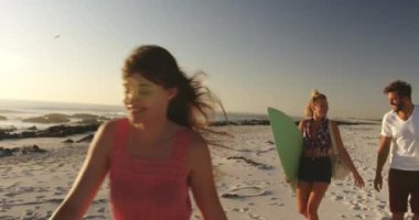 Gün batımında sahilde yürüyen, sörf tahtaları ve plaj çantası taşıyan çok ırklı genç yetişkin arkadaşlardan oluşan çok ırklı bir grubun ön görünümü. Arkadaşlarla yaz eğlencesi, onlar plaj 4k bir yolculuğa vardır