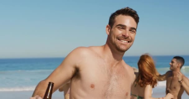 ビールのボトルを持って 彼の友人とビーチで踊っている若い白人男性のクローズアップ 一緒にビーチで夏の楽しみを持っている若い友人4K — ストック動画