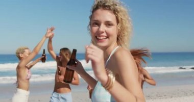 Bir şişe bira tutan ve arkadaşlarıyla sahilde dans eden beyaz bir kadının yakını. Genç arkadaşlar birlikte 4k plajda yaz eğlencesi