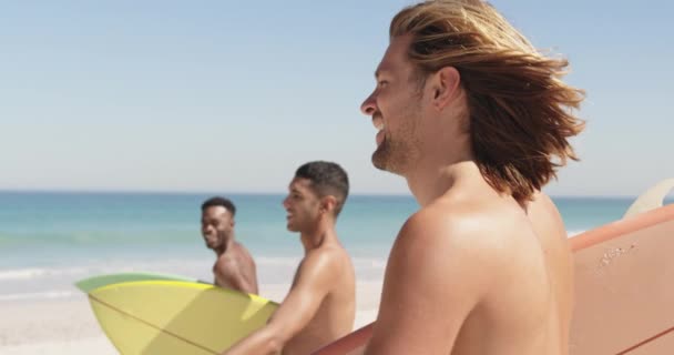 3人の若い成人男性の友人の多民族グループの側面図を閉じて サーフボードを運ぶビーチで走っています 一緒にビーチで夏の楽しみを持っている若い友人4K — ストック動画