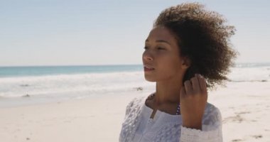 Yakın deniz kenarında bir plaj boyunca yürüyen genç bir Afrikalı-Amerikalı kadın, etrafında dönen ve mesafe 4k içine bakarak