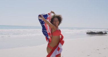Sahilde dans eden, elinde Amerikan bayrağı olan ve gülümseyen genç bir Afro-Amerikan kadını.