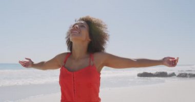 Bir plajda yürüyen gülümseyen genç Afro-Amerikan kadın yakın kollarını kaldırarak ve 4k güneşe yüzünü dönüm
