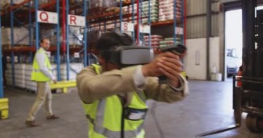 Genç Asyalı bir depo işçisinin, deponun yükleme bölümünde VR kulaklık ve barkod tarayıcısıyla hoplayıp zıplamasını yakından izle.. 