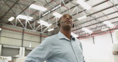 Orta yaşlı Afrikalı Amerikalı bir depo çalışanının depodaki bir kulaklığa konuşmasının düşük açılı görüntüsü..