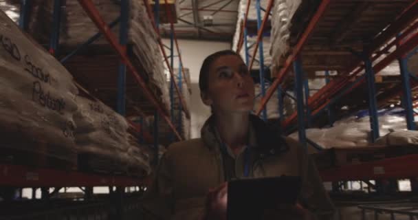 夜に倉庫の廊下をパトロールしている間 タブレットコンピュータを使用して若い白人女性倉庫労働者の正面図を閉じます — ストック動画
