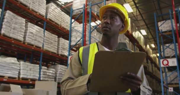 Vue rapprochée d'un jeune ouvrier afro-américain de l'entrepôt écrivant sur un presse-papiers et regardant les étagères de stockage dans un entrepôt . 
