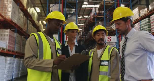 中年の白人女性と男性の倉庫管理者 若いアフリカ系アメリカ人と若いアジア系男性の手動労働者の最前線ビュー倉庫の荷室で会議を持っている 話をし クリップボードを見て — ストック動画