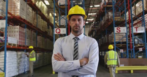 一位中年白种人男性仓库管理员站在仓库装卸工房里 双手叉腰微笑着对着摄像机 头戴黄色硬礼帽的画像 — 图库视频影像