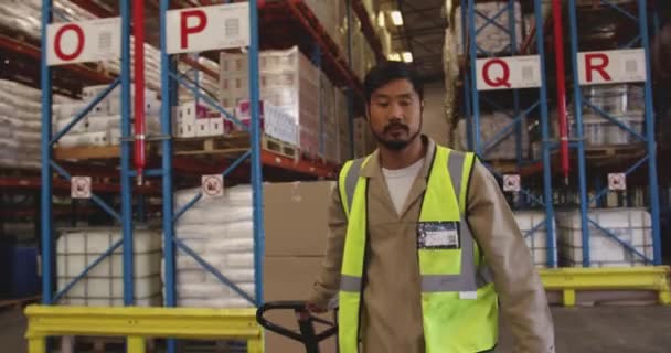 Gros plan d'une femme blanche d'âge moyen gérante d'entrepôt parlant à un jeune ouvrier asiatique déplaçant des boîtes des étagères de stockage sur un chariot. Elle pointe du doigt et lui donne des instructions .