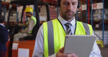 Orta yaşlı beyaz bir erkek depo müdürünü bir tablet bilgisayar ve depo yükleme bölümünde iki yönlü telsiz kulaklığı kullanarak kapatın..
