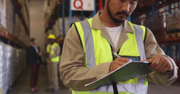 Vue de face gros plan d'un jeune ouvrier d'entrepôt asiatique écrivant sur un presse-papiers dans un entrepôt et sortant d'un tir . 