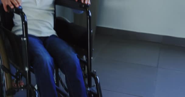 病院の廊下で車椅子でアフリカ系アメリカ人の少年を押す医師の正面図 男の子動揺し 下を見る4K — ストック動画