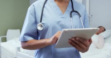 Hastanedeki koğuşta dijital tablet kullanan Afrikalı Amerikalı kadın doktorların ön görüntüsü. Gülümsüyor ve kameraya bakıyor. 