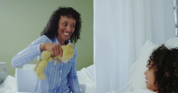 アフリカ系アメリカ人の母親の正面図は 病院で息子にテディベアを与える 彼らは話して笑顔4K — ストック動画