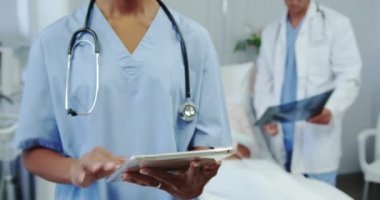 Hastanedeki koğuşta dijital tablet kullanan Afrikalı Amerikalı kadın doktorların ön görüntüsü. Kafkas erkek doktor hastaya röntgen raporu gösteriyor. 
