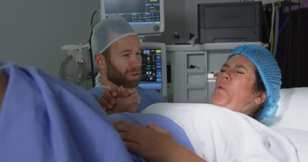 在医院手术室里 白人男子在分娩时安慰孕妇的镜头出现在眼前 他牵着她的手 — 图库视频影像