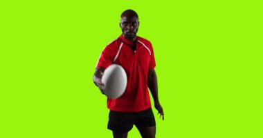 Genç bir Afrikalı Amerikalı erkek rugby oyuncusunun canlandırması, kameraya bakıyor ve rugby topuyla oynuyor ve parlak yeşil arka planda 4k kamerayı işaret ediyor.