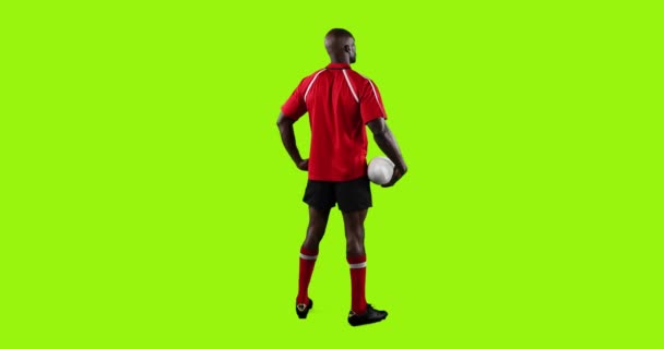 若いアフリカ系アメリカ人男性ラグビー選手の全長リアビューのアニメーション立って明るい緑の背景に彼の手にボールを保持4K — ストック動画