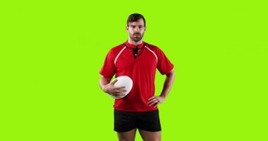 Kafkasyalı genç bir rugby oyuncusunun canlandırması. Kameraya bakıyor ve elinde parlak yeşil bir arka planda topu tutuyor. 4k