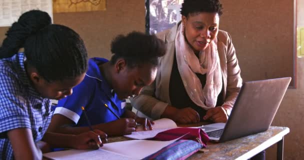 一名非洲中年女教师在一个乡镇小学课堂上用笔记本电脑帮助坐在课桌旁的一名非洲女学生 — 图库视频影像