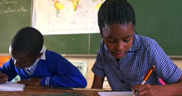 一位年轻的非洲女学生和一名男学生坐在课桌前 面带微笑 写在笔记本上 并在一个城镇小学4K课上认真地听着 — 图库视频影像