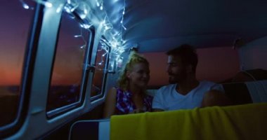 Kafkasyalı bir çiftin karavanda oturduğu ön manzara. Telli ışıklarla aydınlatılmış, konuşan, pencereden dışarı bakan ve geceleri kucaklaşan 4K video.