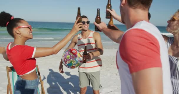 幸せな若い成人の男女の友人が一緒にビーチでぶらぶらして立って ボトルで乾杯し ビールを飲む多民族のグループをクローズアップ 一緒にビーチで夏の楽しみを持っている若い友人4K — ストック動画