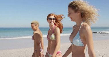 Bikinili bir plajda yürüyen üç mutlu yetişkin bayan arkadaş grubu, video 4K.