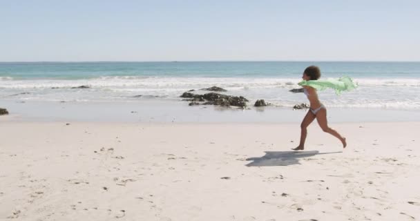 ビーチラップを持って4Kジャンプビーチに沿って走っている若いアフリカ系アメリカ人女性の完全な長さの側面図 — ストック動画