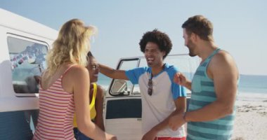 Bir plajda bir kamp minibüsünün açık kapısının yanında duran, konuşup gülen çok ırklı bir yetişkin arkadaş grubunun yakın. Arkadaşları yla plaja Camper Van Yaz Road Trip 4k
