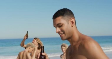 Close up of a young man holding a bottle of beer and dancing on a beach with his friends 4k