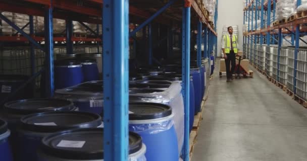 Vue de face pleine longueur d'un jeune homme asiatique déplaçant des boîtes sur un chariot dans un couloir entre des étagères dans un entrepôt . 