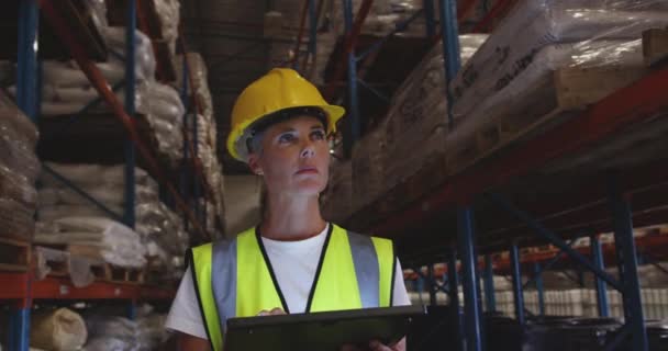 中年の白人女性の倉庫労働者の正面図を閉じる彼女は夜に倉庫の廊下をパトロールしながら 黄色のハード帽子を着用し タブレットコンピュータを使用して — ストック動画