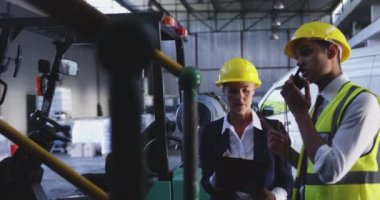 Orta yaşlı beyaz bir kadın depo müdürü ve bir depo yükleme koyunda konuşan genç bir Asyalı erkek depo yöneticisi yakın. İki yönlü bir radyoda konuşuyor. 4k