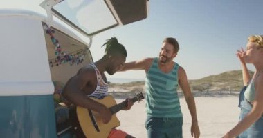 Afrikalı Amerikalı bir adam gitar çalar, kumsaldaki arkadaşları, videosu