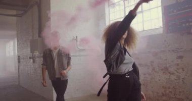 Boş bir depoda bir kalça genç karışık ırk adam ve bir kalça genç Kafkas kadın Ön görünümü, yürüyüş, kadın bir el bombası tutan ve etrafında dönüyor