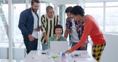 Modern bir ofisteki bir toplantıda dizüstü bilgisayarın etrafında duran çeşitli yaratıcı profesyonellerden oluşan bir grubun ön görüntüsü