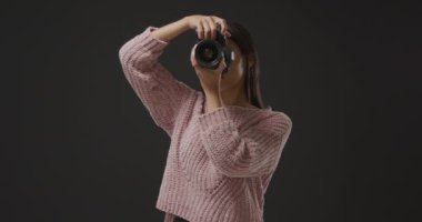 Beyaz beyaz bir kadının dijital Slr fotoğraf makinesiyle dikey bir fotoğraf çekerek kamera ekranında ona bakıp gülümsediği ön görüş