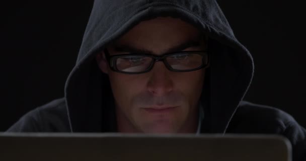 黒いパーカーとメガネを身に着けた若い白人男性の正面図を閉じ コンピュータを見下ろして入力し メガネに映る画面の反射 — ストック動画