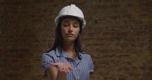 白いハードハットをかぶった若い白人女性が手を平らにして手を上げて まるで物体を持ち それを見下ろすかのように 正面図を閉じる — ストック動画