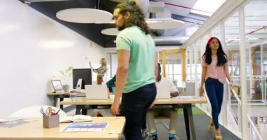 Kafkasyalı genç bir erkek yöneticinin ayakta durup, konuşurken ve beşlik çakarken genç bir Afrikalı Amerikalı erkek yaratıcı ve tesettürlü genç bir Asyalı kadın bilgisayar kullanarak sıralarda otururken