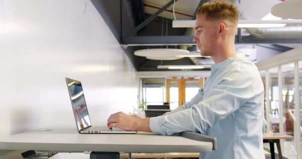 デスクで働く多様な創造的な同僚のグループと 現代のオープンプランオフィスでトレッドミルを歩き ラップトップコンピュータで作業している若い白人男性の創造的な仕事の終わりをサイドビュー — ストック動画