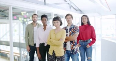 Modern bir açık plan ofisinde kameraya bakan bir grup çok ırklı yaratıcı profesyonelin portresi.