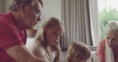 Son sınıf beyaz bir erkek ve kadının yan görüntüsü. Torunları ve torunlarıyla birlikte oturma odasında boyuyorlar.