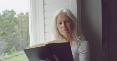 Bir kitap okuma ve bir pencereden dışarı bakarak düşünceli bir üst düzey Kafkas kadın yan görünümü yakın