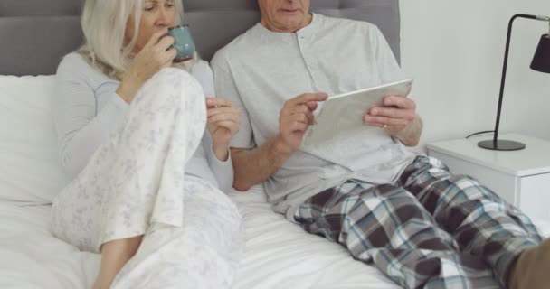 ベッドの中の白人女性と男性の正面図 コーヒーカップを保持し タブレットコンピュータを使用して — ストック動画