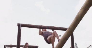 Bir acemi birliği eğitim seansında arka planda başka bir katılımcıyla açık hava spor salonunda çerçeveye tırmanan beyaz bir kadının ön görüntüsü.